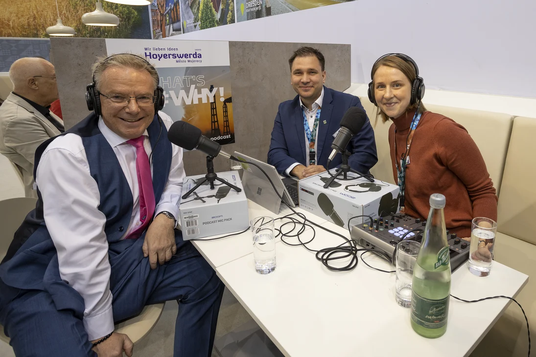 Drei Personen nehmen einen Podcast auf und haben Kopfhörer auf.